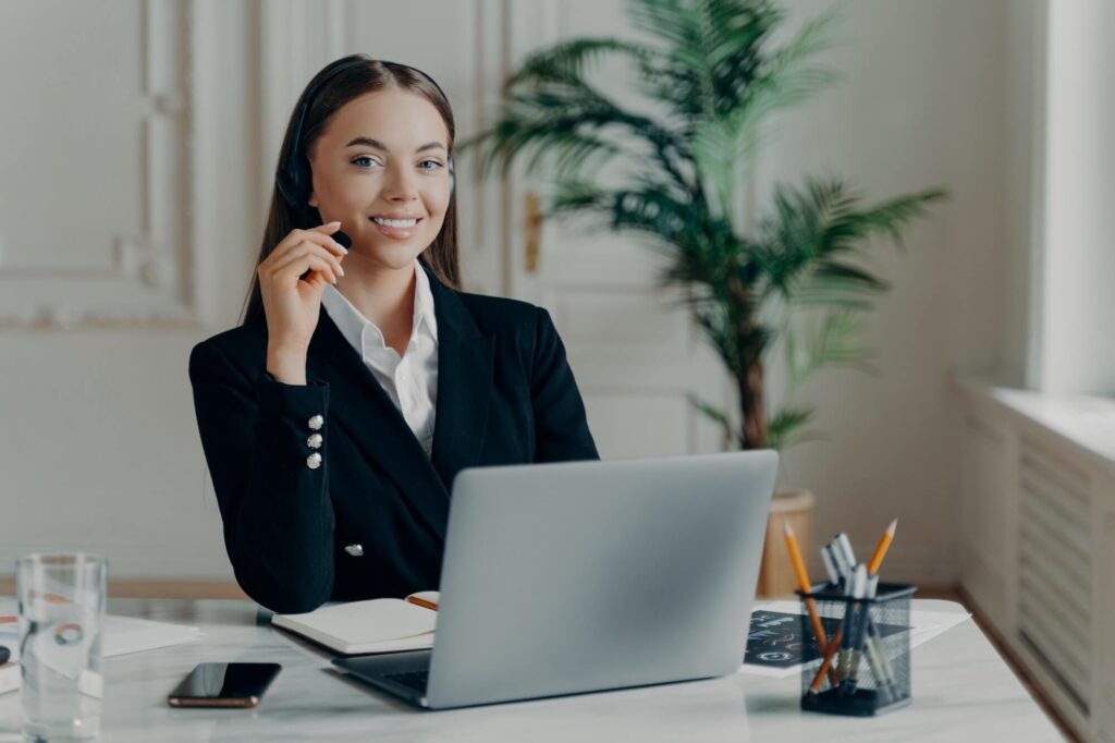 Female office worker in headset smiling at camera during online meeting